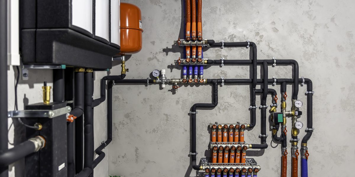 Chaufferie moderne : collecteur, vannes et vase d'expansion rouge sur un mur gris